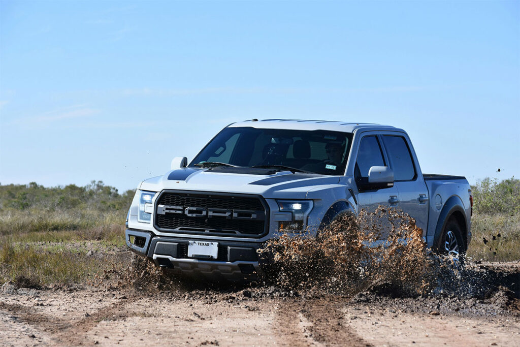 Silver Ford pickup truck splashing through muddy terrain