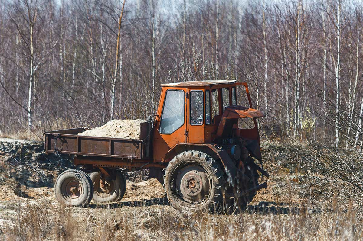 Old orange tractor hauling sand in rural field