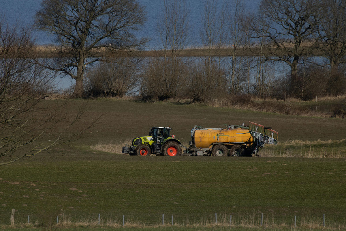 Tractor pulling yellow tank in farmland field