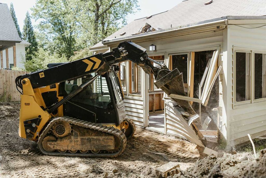 yellow skid steer demolishing wall of suburban house