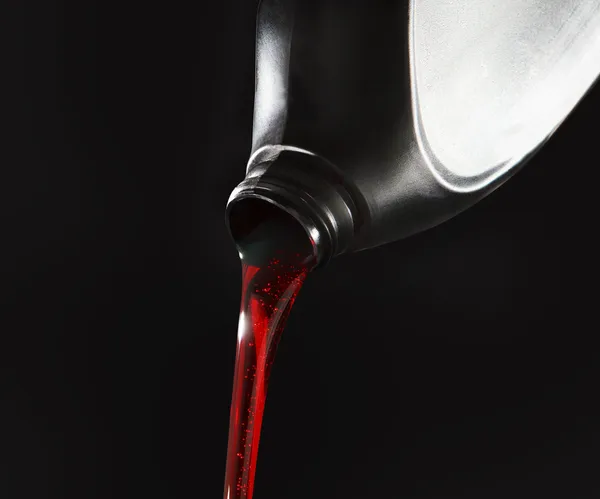 Red diesel being poured out of a black container on black background